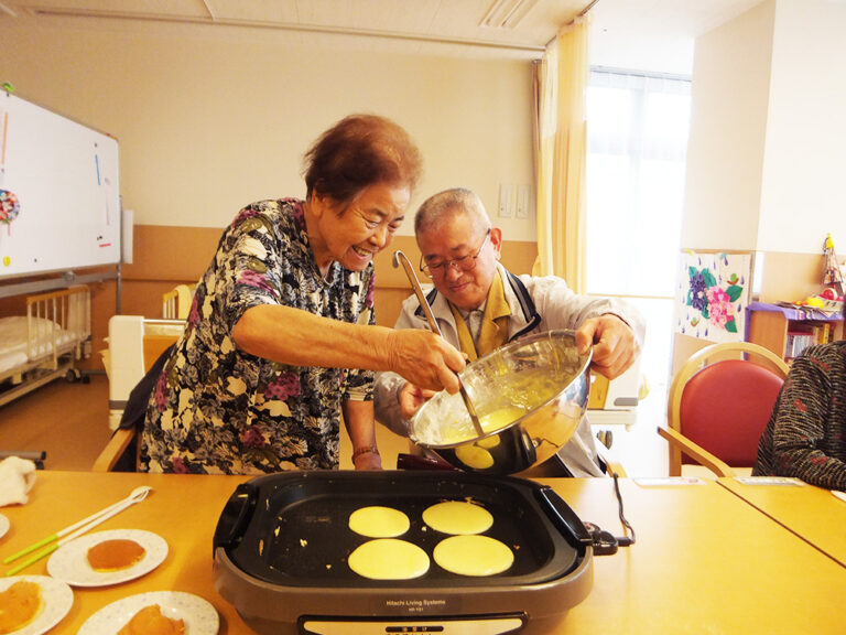 入居者と職員がホットプレートで調理するレク活動の様子