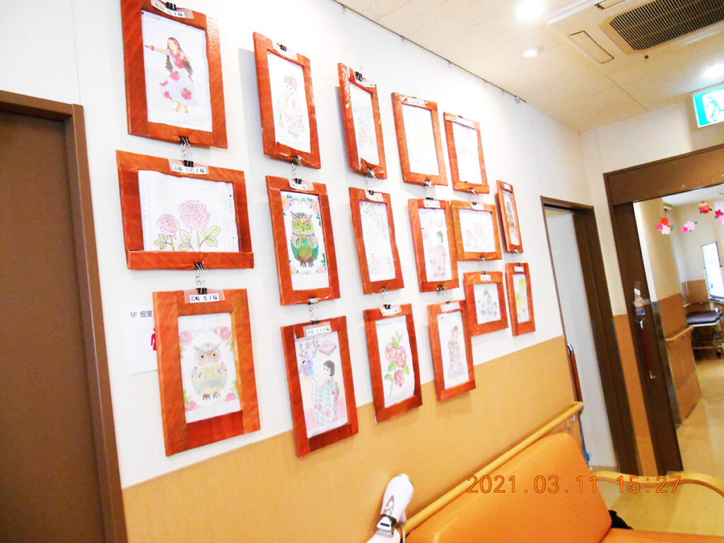 廊下に展示された入居者の絵画作品。赤いフレームで複数の作品が壁に飾られている。